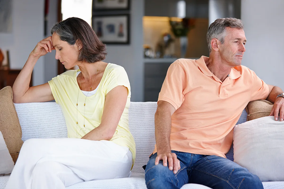 A couple sitting on a couch ignoring each other, showing emotional distance during menopause