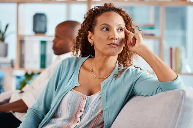 A frustrated woman sitting apart from her husband on a couch, illustrating strain during menopause and divorce
